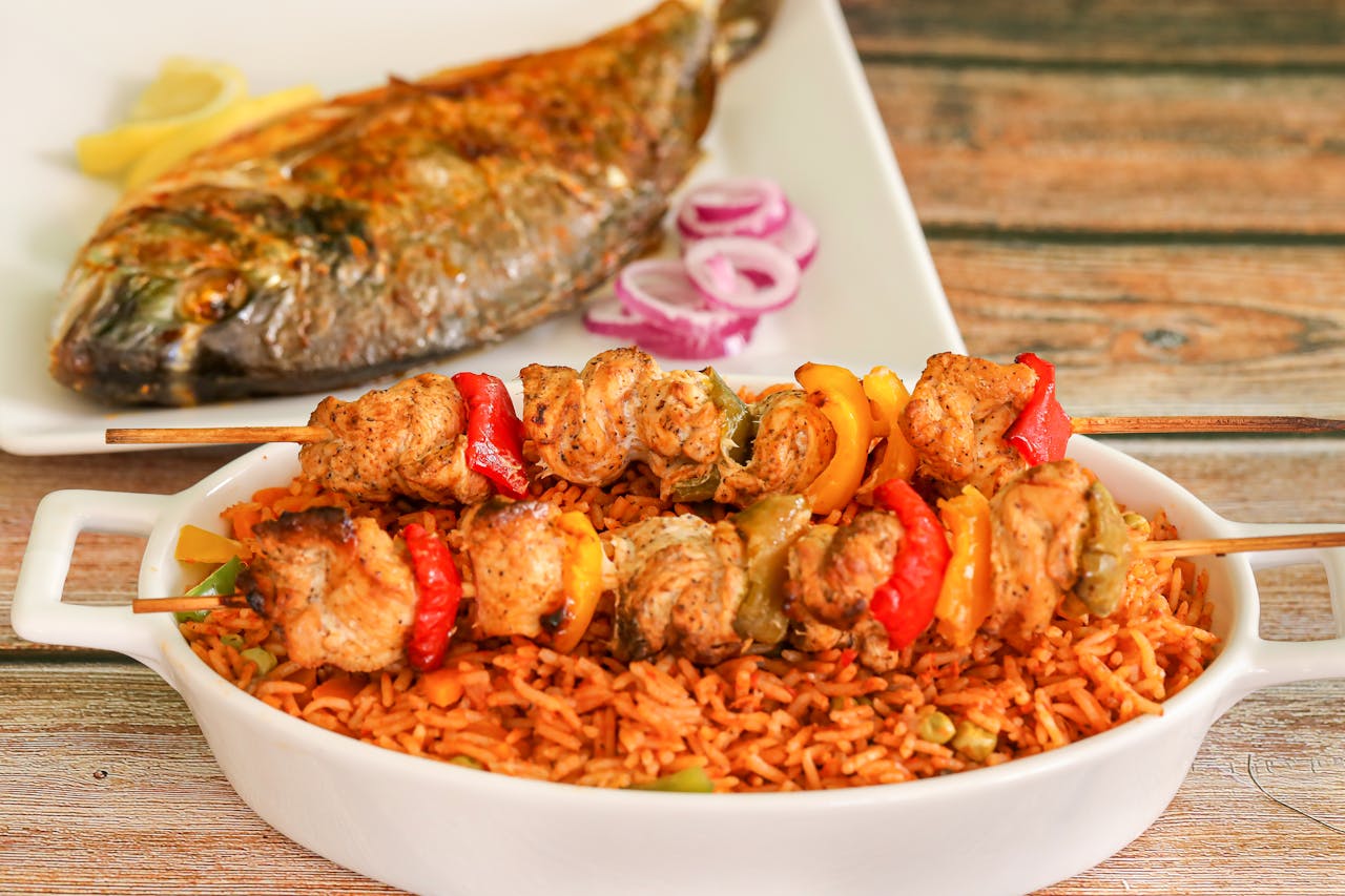 services-04 Close-up of flavorful Nigerian jollof rice with grilled chicken skewers and roasted fish.