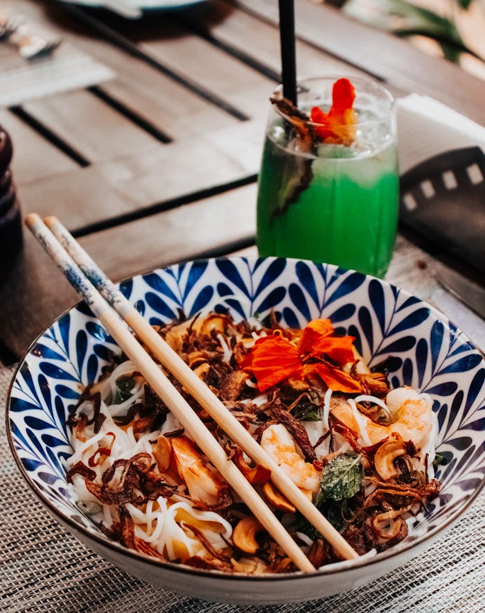 heros-img Colorful noodle dish paired with a refreshing green cocktail, set outdoors in Nairobi, Kenya.