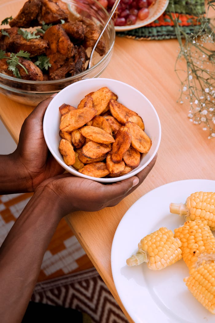 about-us A vibrant African meal featuring fried plantains, chicken, and corn on a wooden table.